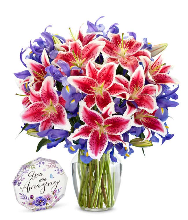pink and white stargazer lilies with blue/purple iris in a clear glass vase