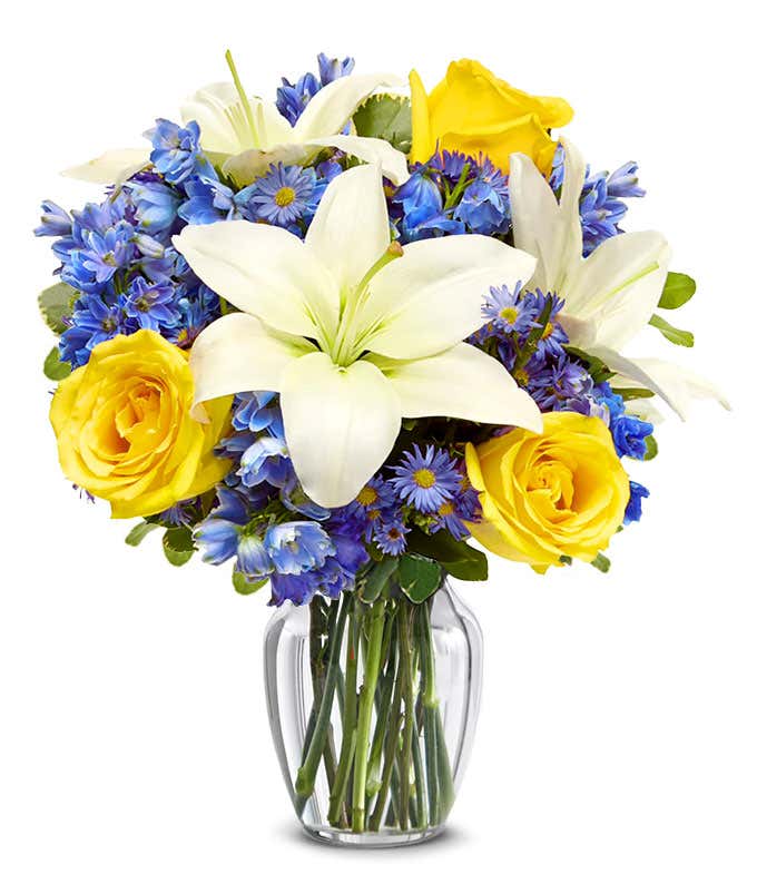 An elegant floral arrangement featuring white Asiatic lilies, yellow roses, blue delphinium, and purple Monte Casino, optionally arranged in a glass vase. This vibrant mix offers a stunning and colorful display.