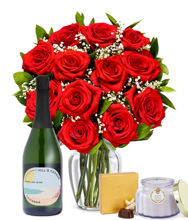 One Dozen Red Roses in Clear Glass Vase with box of chocolates, a bottle of sparkling wine, and candle