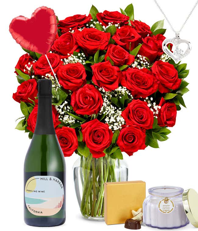 Two Dozen Red Roses in a clear glass vase with a box of chocolates, a silver heart necklace, red heart mylar balloon, a bottle of sparkling wine, and a dahlia &amp; orchid scented candle