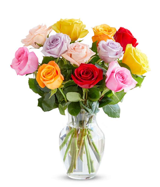 A bouquet of multicolored roses in a clear vase, featuring red, pink, orange, yellow, peach, and lavender blooms, arranged with green leaves for a vibrant and cheerful display.