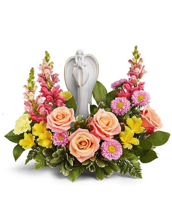Arrangement featuring peach roses, yellow alstroemeria, yellow carnations, hot pink snapdragons, pink asters, and floral greenery with a ceramic figurine atop the arrangement 