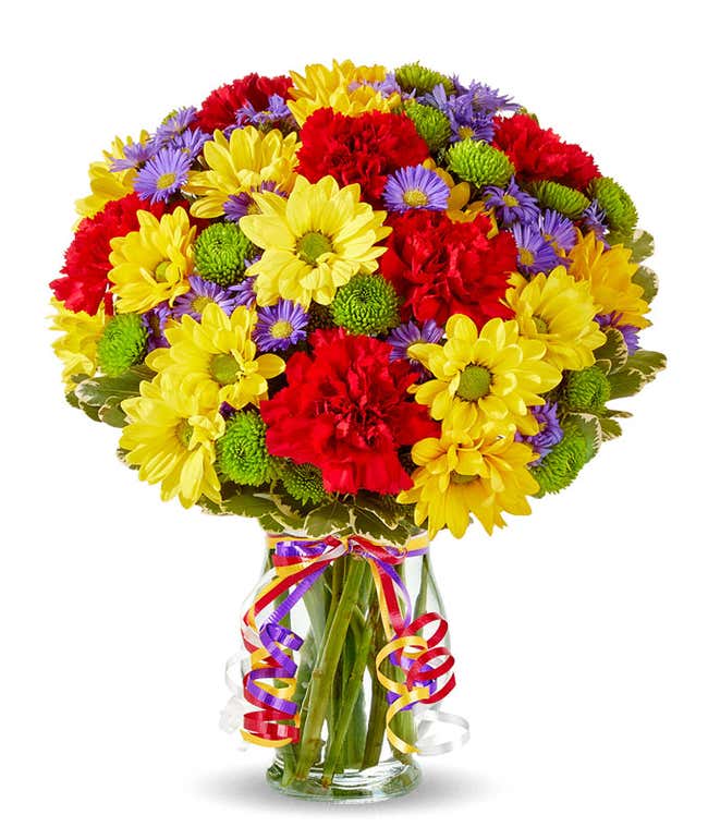 Yellow daisies, red carnations and green button poms in a glass vase