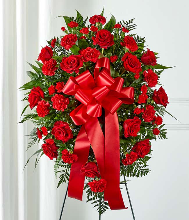 A heartfelt standing spray featuring red roses and carnations with floral greens, arranged by your local florist and hand-delivered with a decorative red bow.