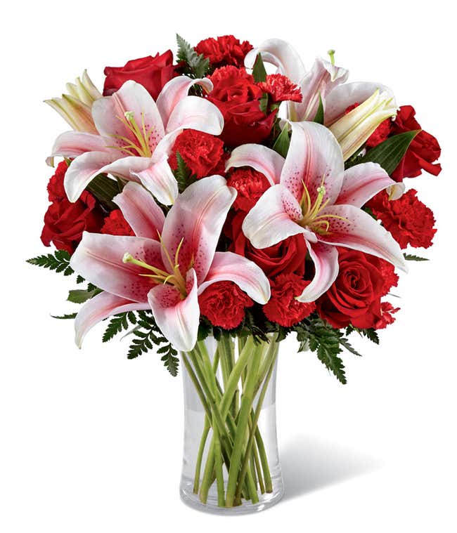 Elegant bouquet featuring red roses, red spray roses, and stargazer lilies in a clear glass vase. A romantic floral arrangement perfect for Valentine&rsquo;s Day, anniversaries, or expressing heartfelt affection.