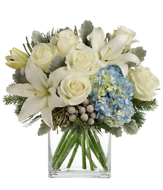 A bouquet of blue hydrangea with white lilies, roses, and berries. Filled out with evergreens and dusty miller.