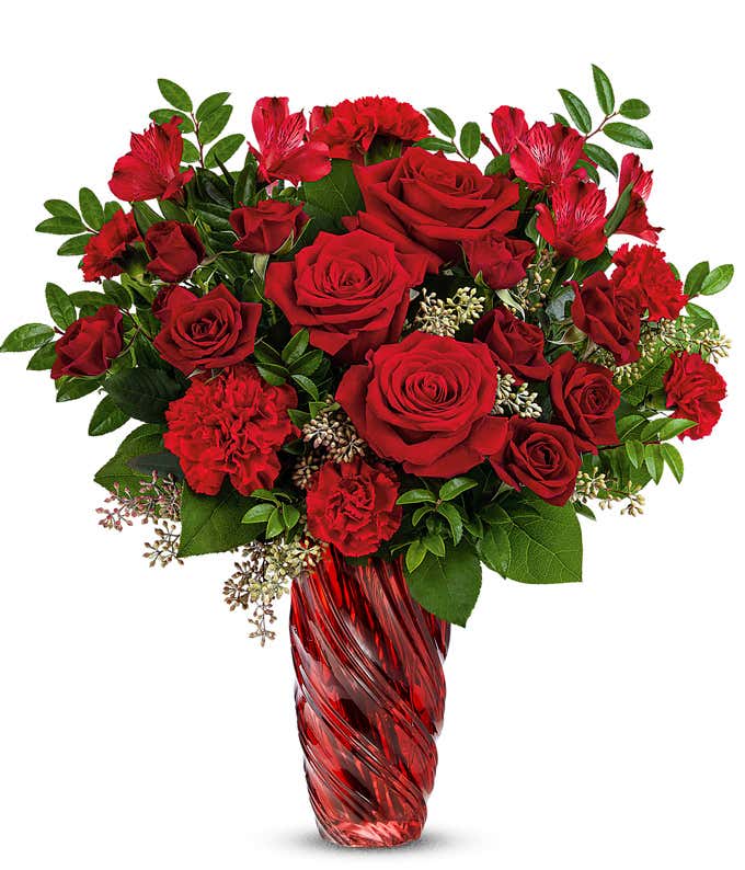 Full arrangement of red roses and carnations in a tall red swirl vase