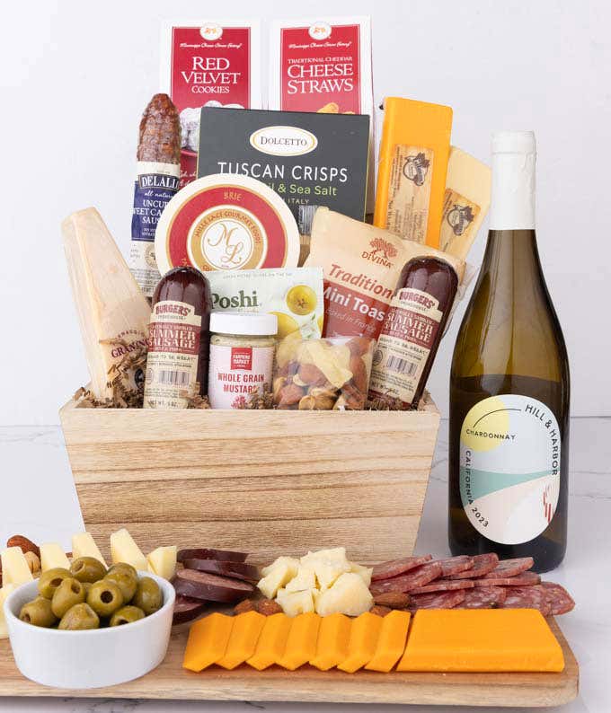 Wooden basket filled with 4 cheeses, 3 sausages, crackers, cookies, nuts, mustard, olives and crisps alongside a bottle of Hill & Harbor Chardonnay.