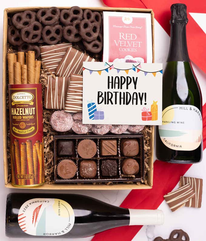 A gift box with chocolate pretzels, chocolate graham crackers, red velvet cookies, hazelnut wafer rolls, an 8 piece box of chocolates, 2 bottles of wine and a Birthday message card.