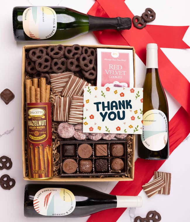 A gift box with chocolate pretzels, chocolate graham crackers, red velvet cookies, hazelnut wafer rolls, an 8 piece box of chocolates, 3 bottles of wine and a Thank You message card.