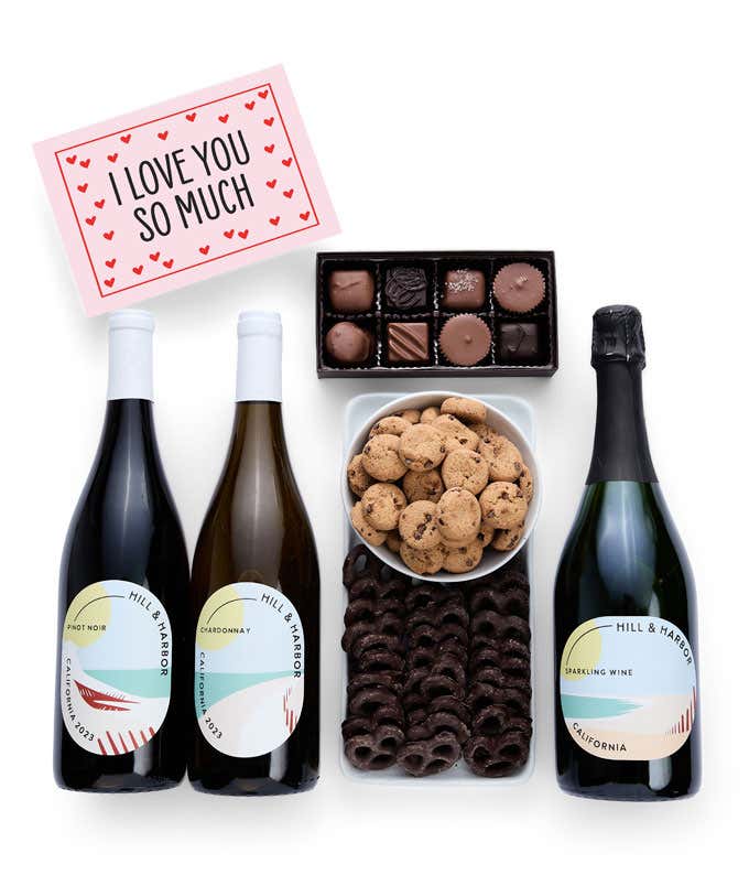 A gift box with chocolate pretzels, chocolate graham crackers, red velvet cookies, hazelnut wafer rolls, an 8 piece box of chocolates, 3 bottles of wine and an I Love You message card.